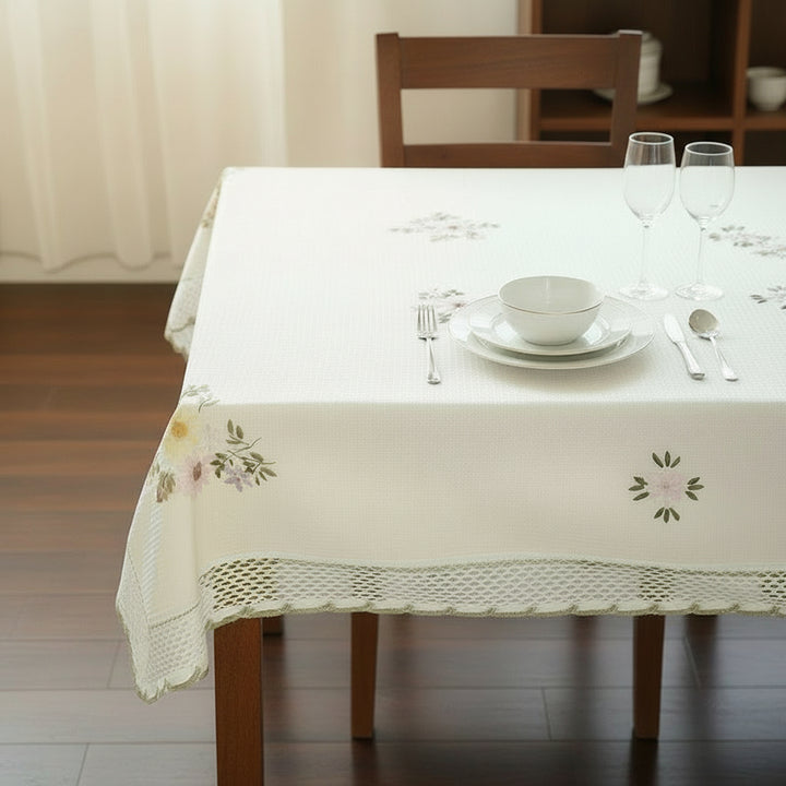 Tablecloth with floral embroidery on a wooden table with plates and flowers.