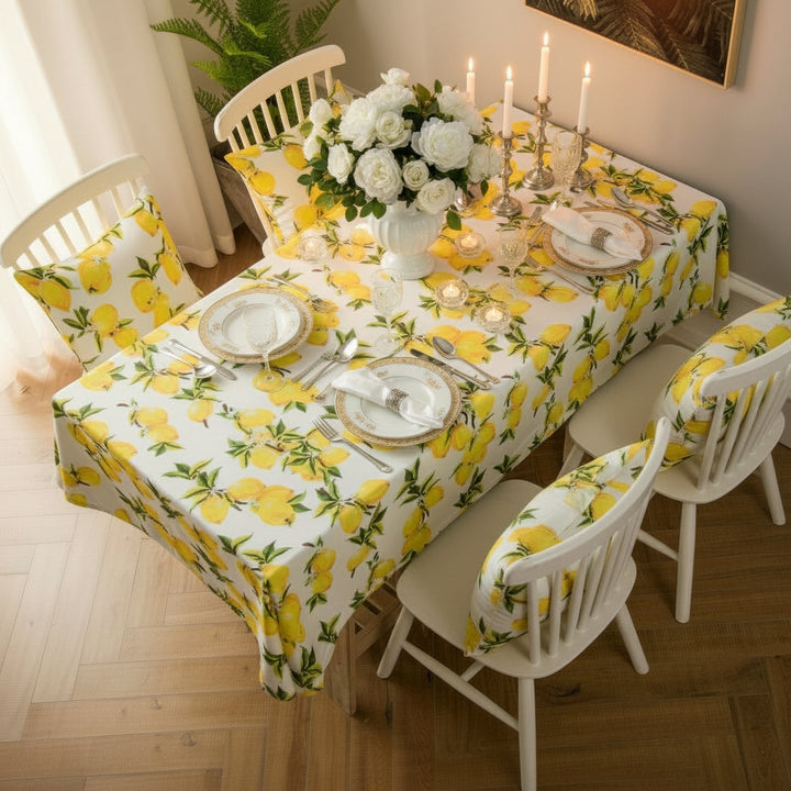 Dining table with lemon-patterned tablecloth and chairs in a bright room.