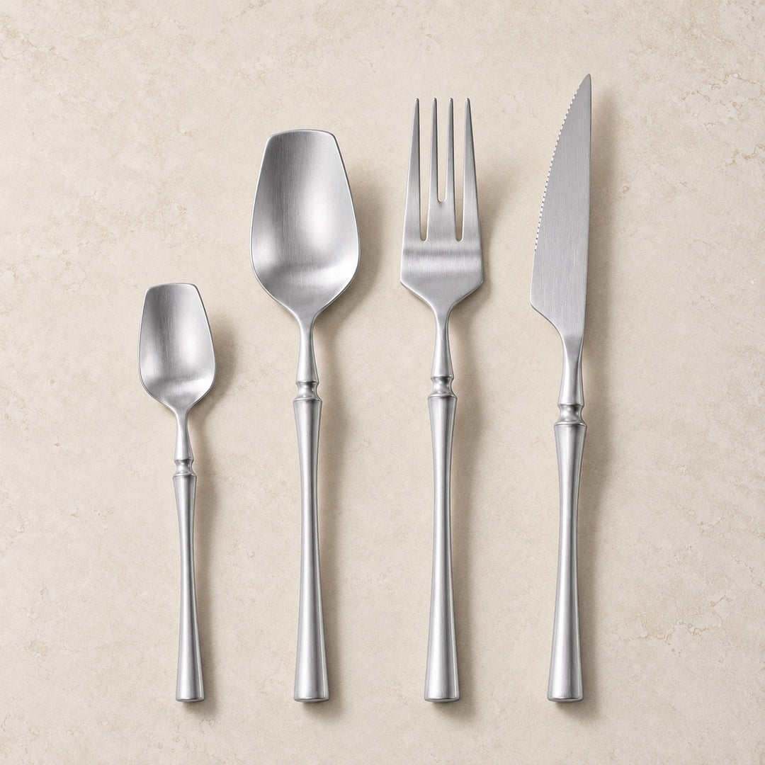 Four-piece stainless steel cutlery set with elegant handles, including a teaspoon, soup spoon, dinner fork, and dinner knife, arranged vertically on a textured beige background.