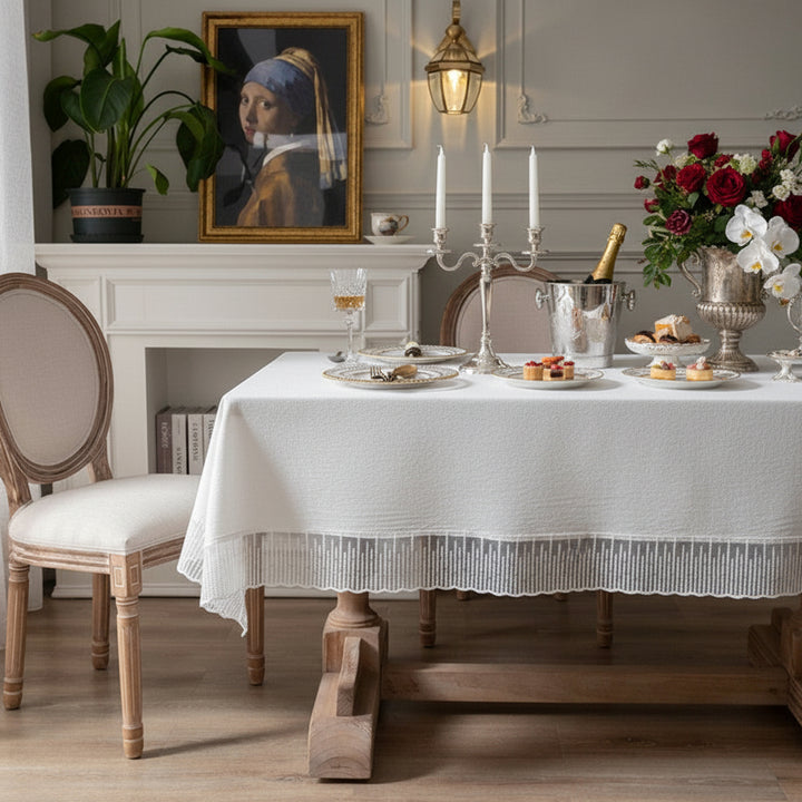 Dining room with a table set for a meal, featuring a white lace tablecloth and, painting on the wall.
