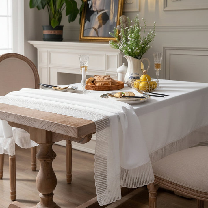 Dining table set with a white lace tablecloth, plates, and glasses in a cosy room.