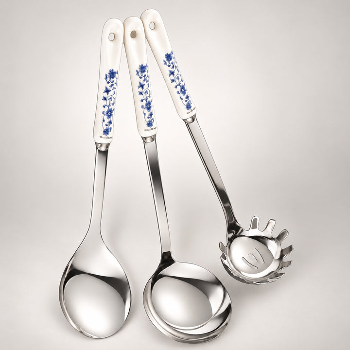Three stainless steel kitchen utensils with white ceramic handles decorated with a blue floral pattern, arranged on a light grey background.