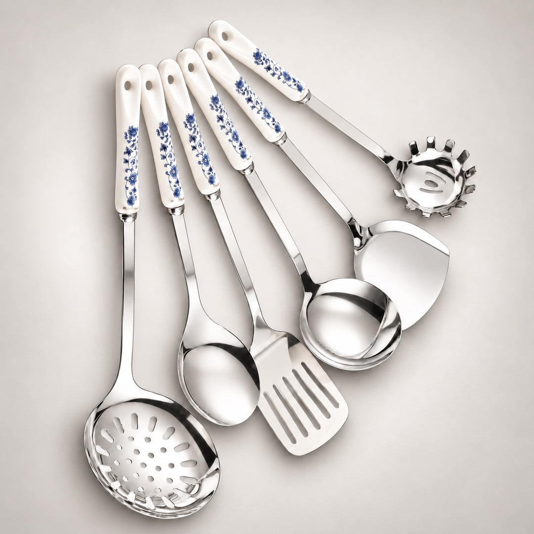 A set of six stainless steel kitchen utensils with white ceramic handles decorated with a blue floral pattern, arranged on a light grey background.