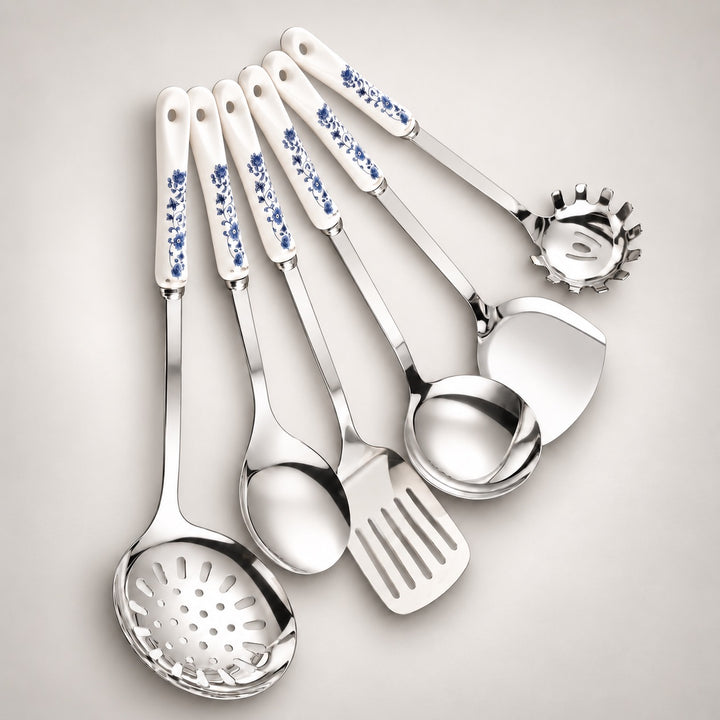 A set of six stainless steel kitchen utensils with white ceramic handles decorated with a blue floral pattern, arranged on a light grey background.