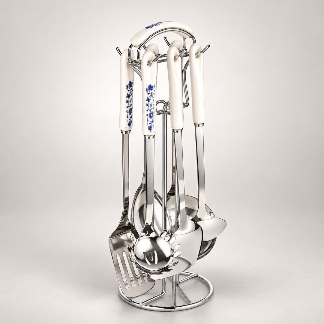 A stainless steel kitchen utensil set with white ceramic handles decorated with blue floral patterns, displayed on a matching metal stand against a light grey background.