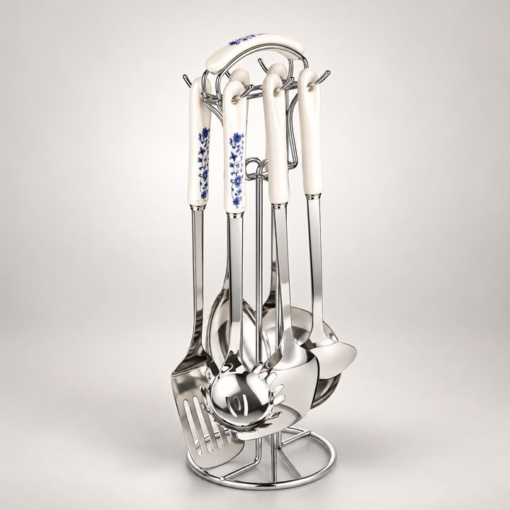 A stainless steel kitchen utensil set with white ceramic handles decorated with blue floral patterns, displayed on a matching metal stand against a light grey background.