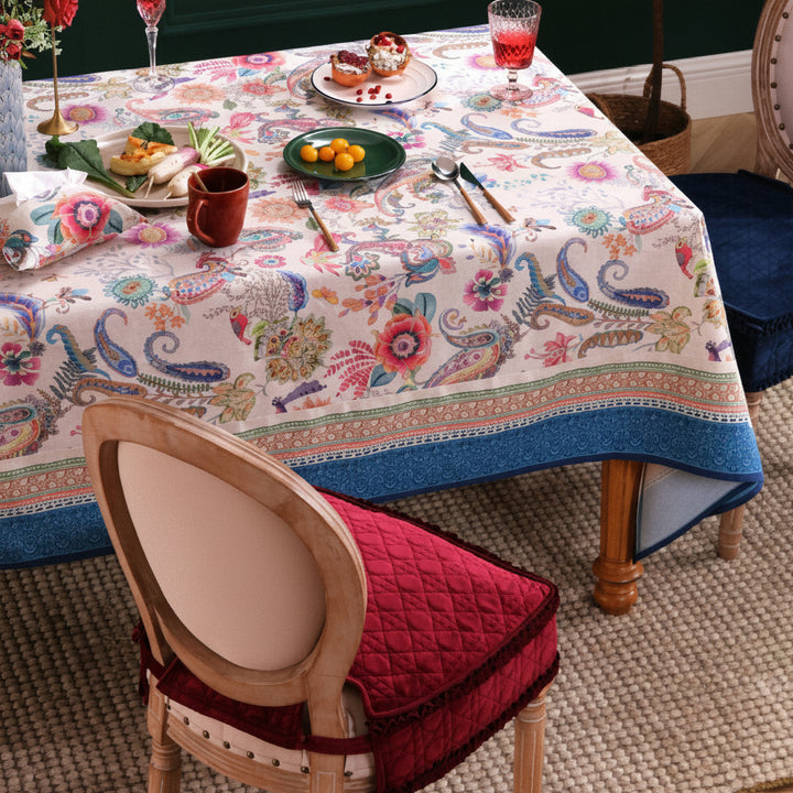 Colorful paisley tablecloth on a dining table with chairs and food.