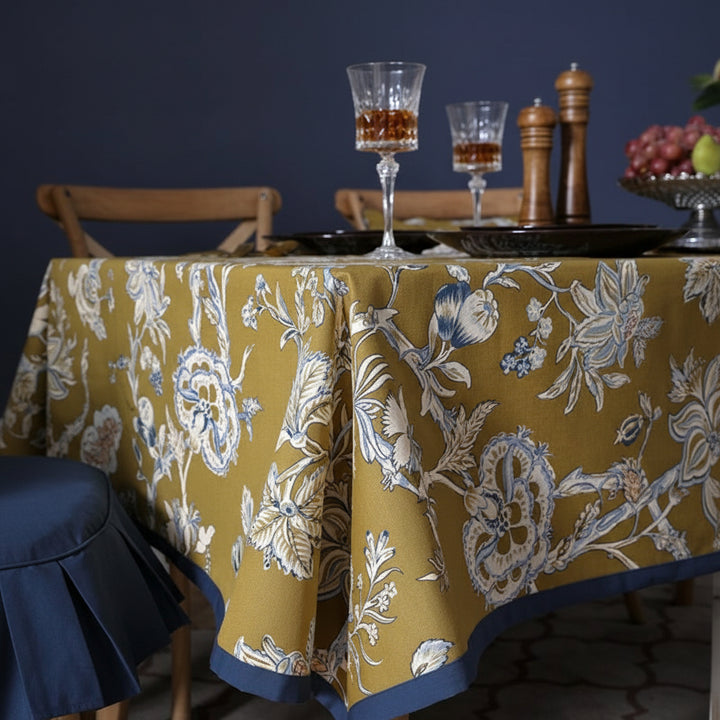Dining table with a floral-patterned tablecloth, glasses, and fruit on a dark background.