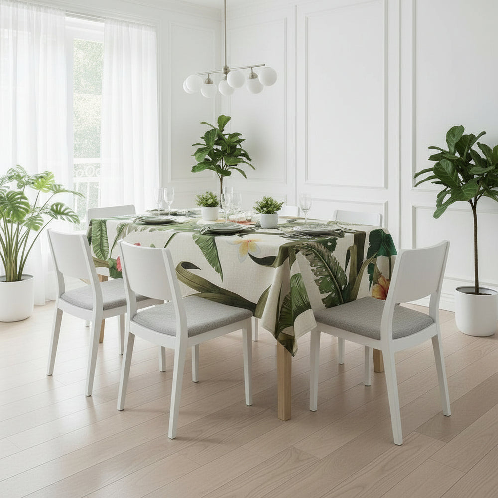 Dining room with a table set for four, featuring a leaf-patterned tablecloth and potted plants.