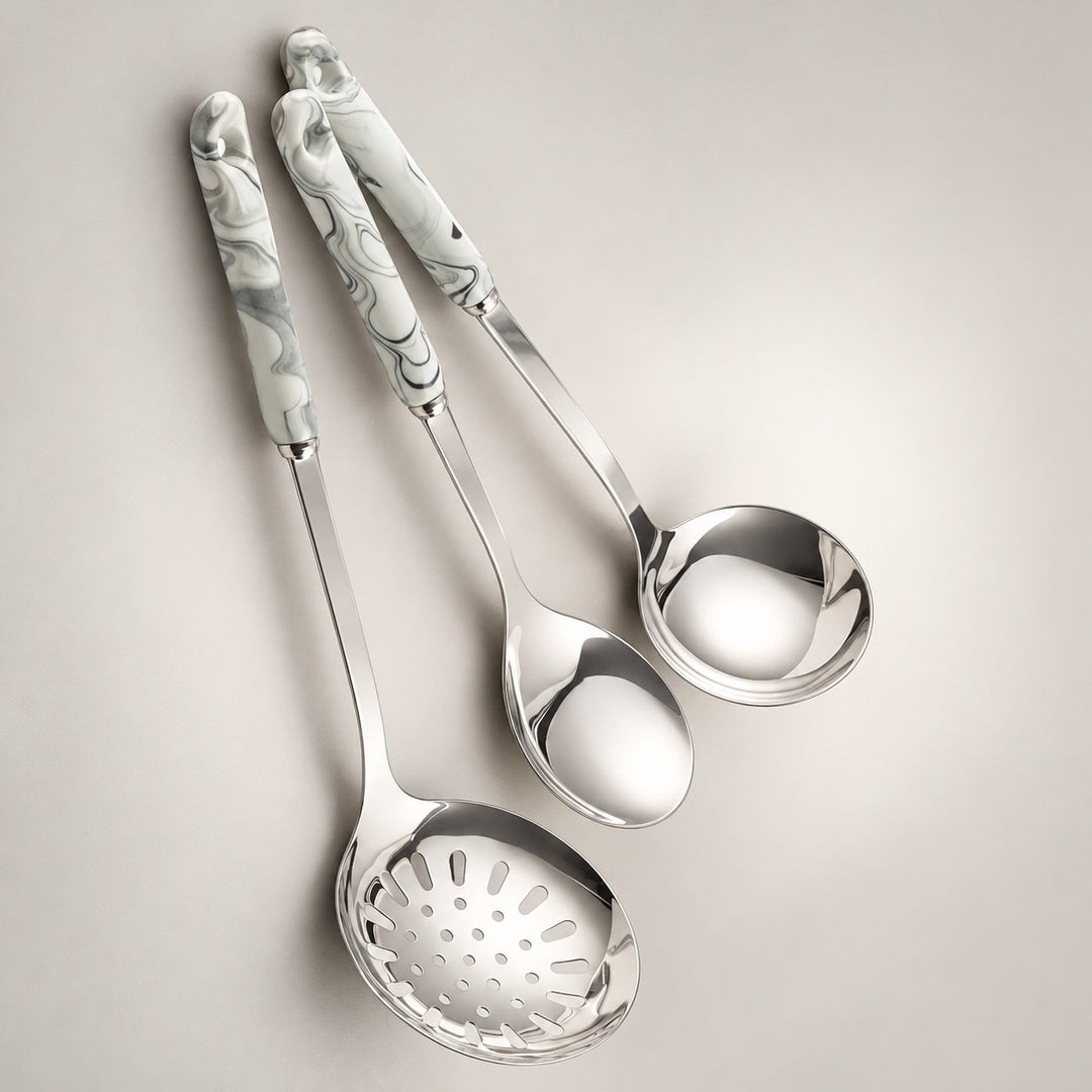 Three stainless steel kitchen serving utensils with grey marbled handles, arranged diagonally on a light grey background.