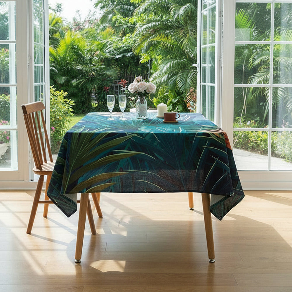 Dining table with a tropical leaf patterned tablecloth in a bright room with large windows.