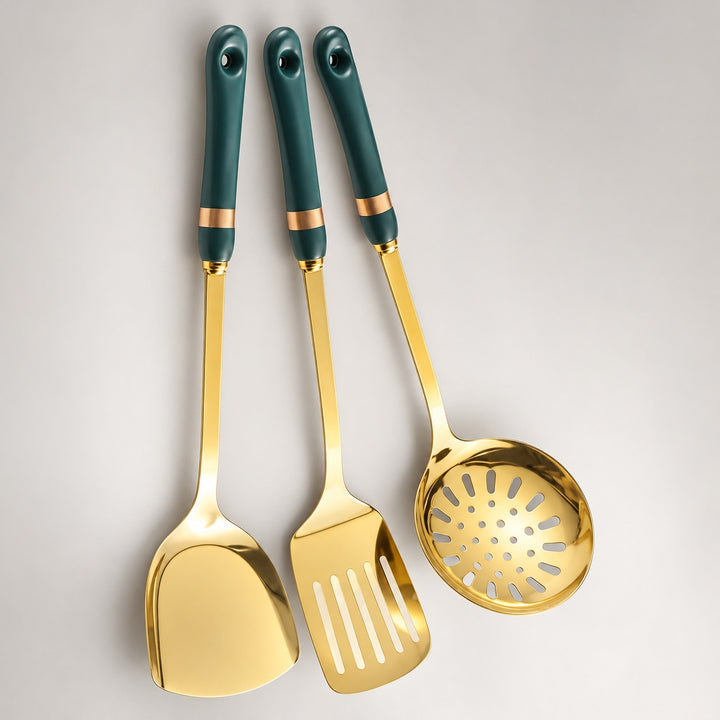 Three stainless steel kitchen utensils with dark green handles and gold accents, including a spatula, a slotted spoon, and a turner, arranged vertically on a light gray background.