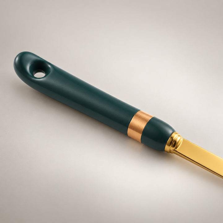 A close-up of a kitchen utensil handle with a dark green body, a metallic gold band, and a gold blade, shown on a light gray background.