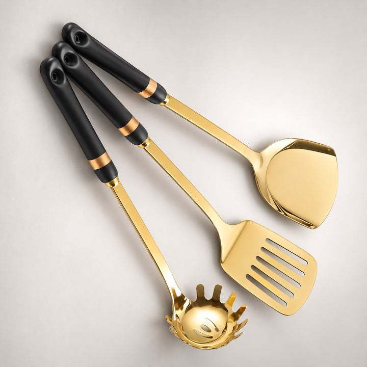 Three gold kitchen utensils with black handles and gold bands, arranged diagonally on a light gray background.