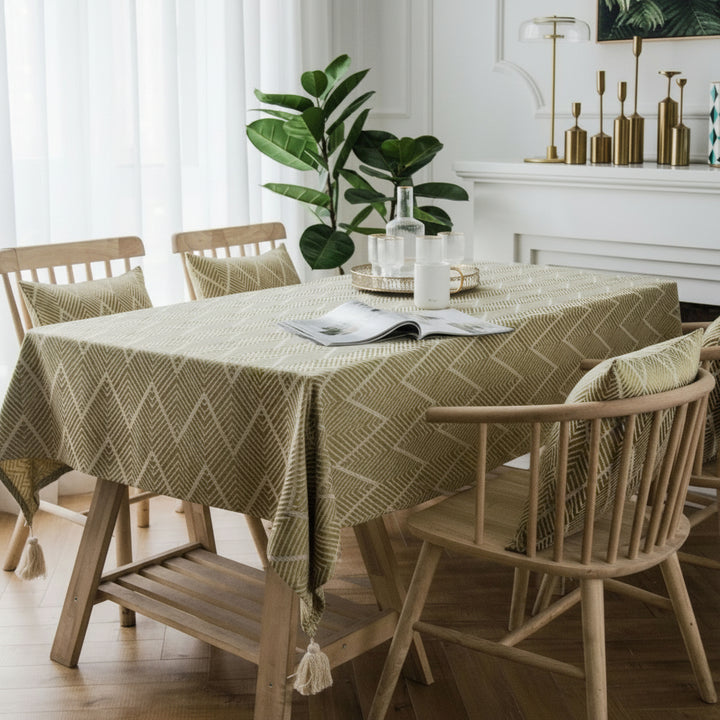 Dining room with a round table covered by a yellow patterned tablecloth, surrounded by wooden chairs.