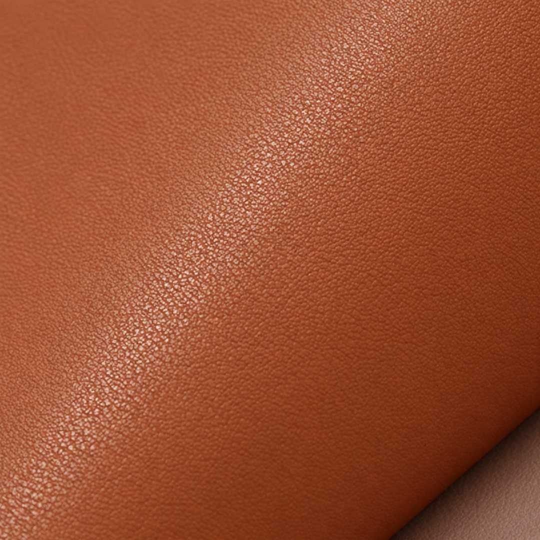 A close-up of a warm brown pebbled faux-leather placemat material with a soft diagonal fold showing the texture and colour.