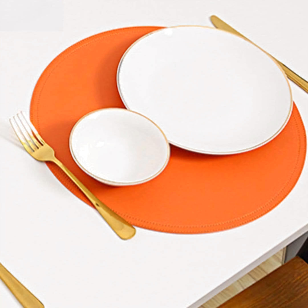 Orange leather placemat and coaster with a white plate and cup on a white table.