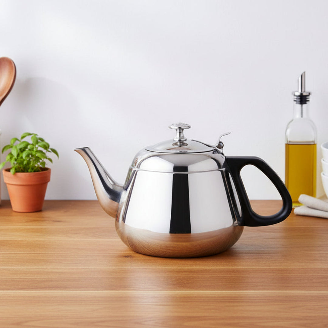 Stainless steel teapot on a wooden surface with decorative items.