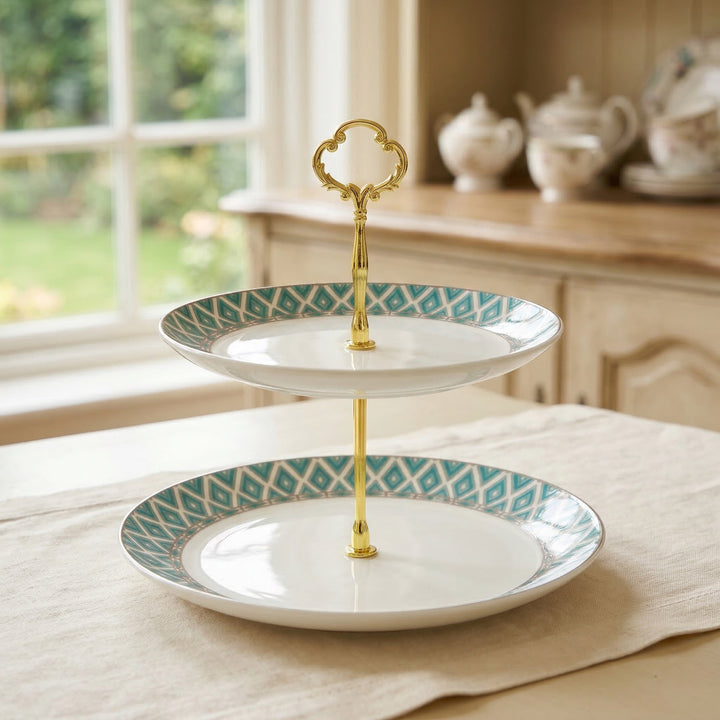 The Edwardian two-tiered bone china cake stand with gold accents on a table in a bright room.
