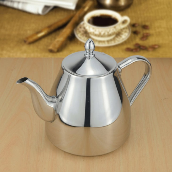 Silver teapot on a wooden surface with a blurred background of coffee cup and cinnamon sticks.